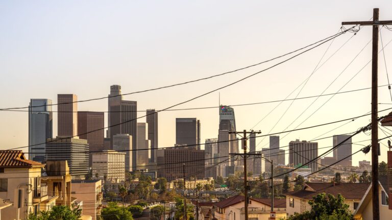 Capture of downtown Los Angeles skyline under a warm sunset, showcasing iconic skyscrapers and urban landscape.